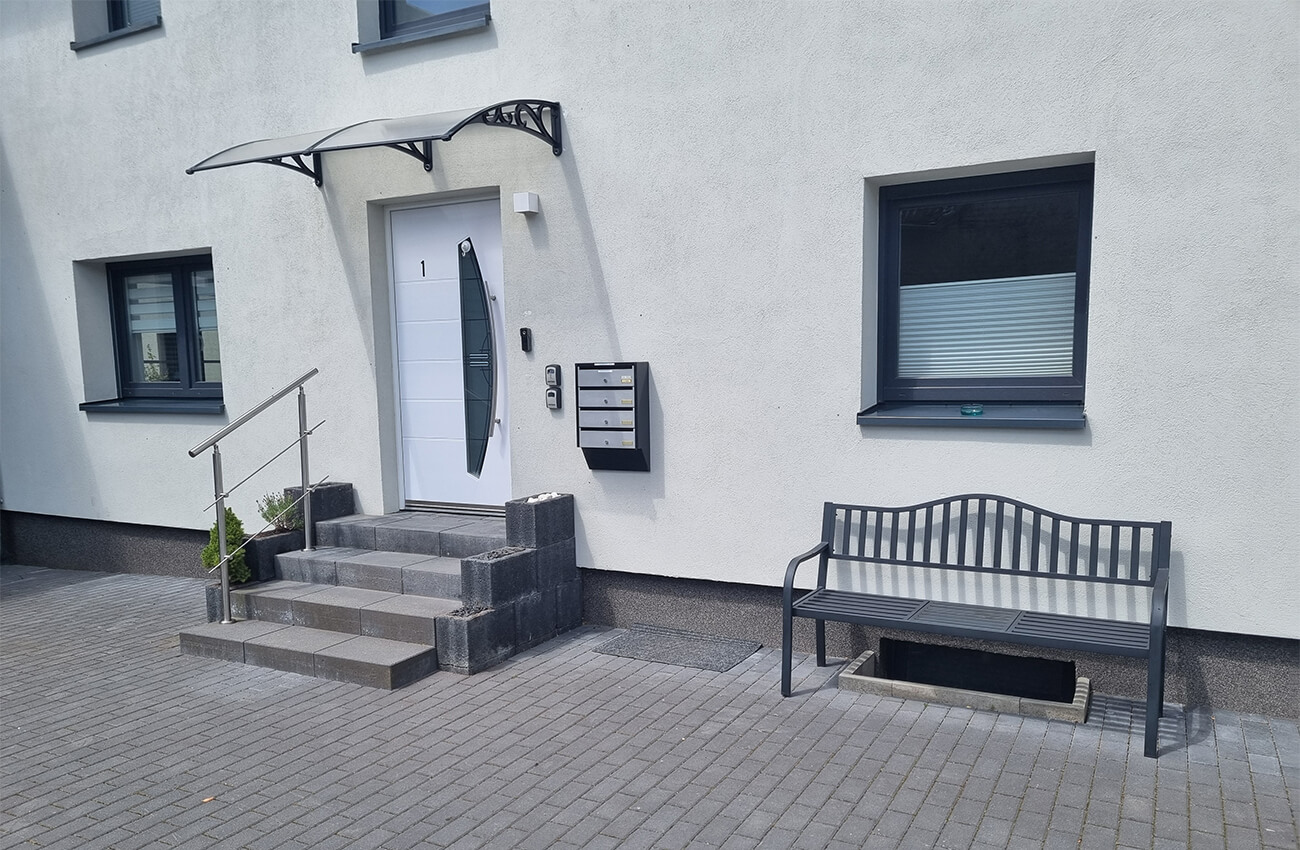 Moderner Hauseingang mit weißer Tür, Briefkästen und Sitzbank vor dem Apartmenthaus