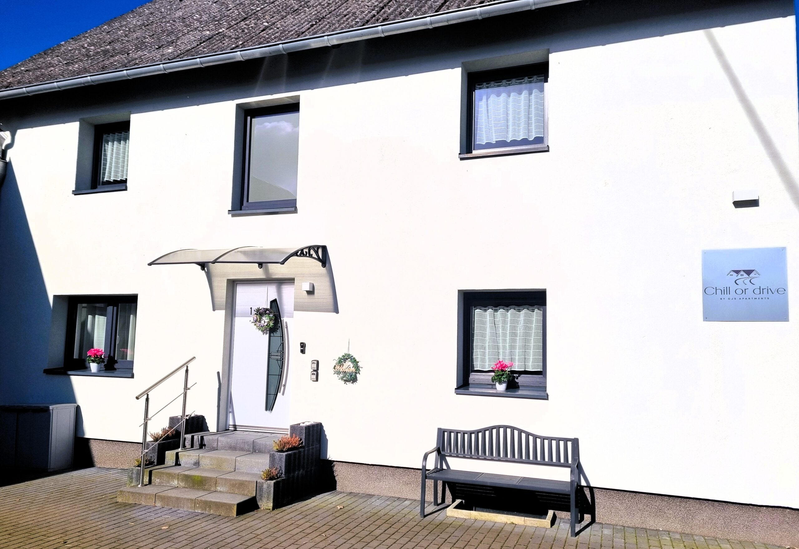 Eingangsbereich mit Logo, Sitzbank und Parkplatz